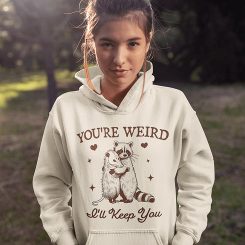 Celebrate the beauty of quirky connections with our comfy hoodie, featuring an adorable illustration of a raccoon and possum sharing a heartwarming hug.
